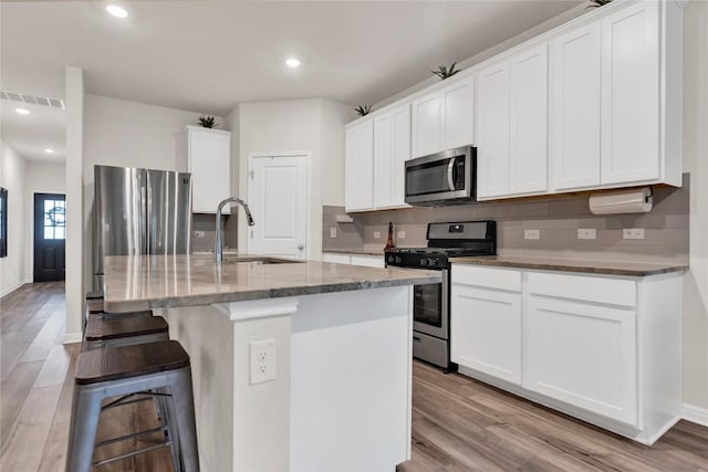 202 Grapefruit Rd, Hutto, TX 78634 - kitchen featuring appliances with stainless steel finishes, light wood-style floors, an island with sink, stone countertops, and recessed lighting