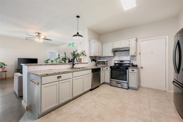 903 Thackeray Ln, Pflugerville, TX 78660 - kitchen featuring appliances with stainless steel finishes, a peninsula, under cabinet range hood, backsplash, and light stone countertops