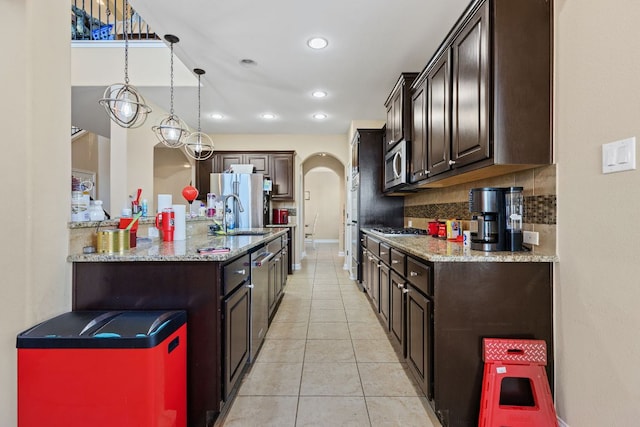 3604 Rosalina Loop, Round Rock, TX 78665 - kitchen with appliances with stainless steel finishes, dark brown cabinets, light tile patterned flooring, light stone counters, and arched walkways