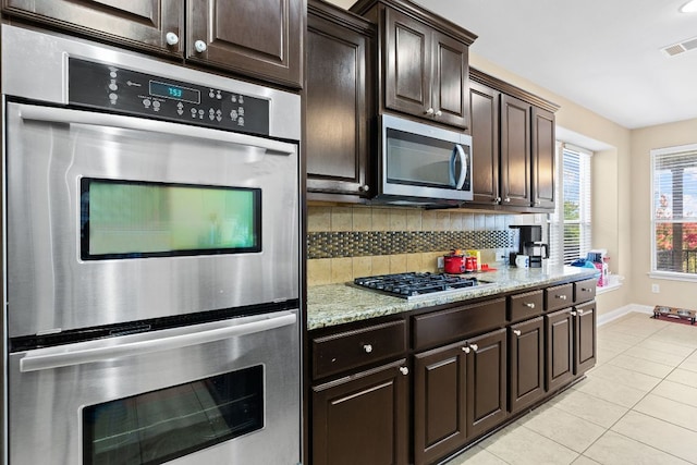 3604 Rosalina Loop, Round Rock, TX 78665 - kitchen featuring appliances with stainless steel finishes, light tile patterned floors, decorative backsplash, dark brown cabinetry, and light stone countertops