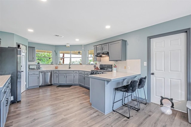 255 Mesquite Dr, Cedar Creek, TX 78612 - kitchen with appliances with stainless steel finishes, under cabinet range hood, a peninsula, gray cabinets, and a breakfast bar area