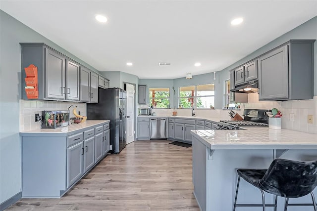 255 Mesquite Dr, Cedar Creek, TX 78612 - kitchen with stainless steel appliances, a peninsula, gray cabinets, under cabinet range hood, and a kitchen bar
