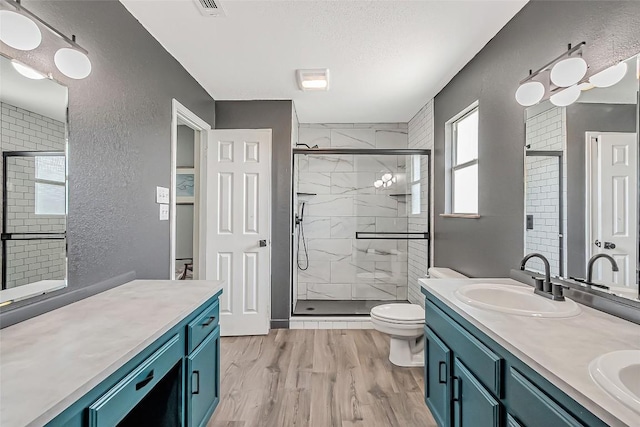 255 Mesquite Dr, Cedar Creek, TX 78612 - bathroom featuring a textured wall, double vanity, a shower stall, wood finished floors, and a textured ceiling