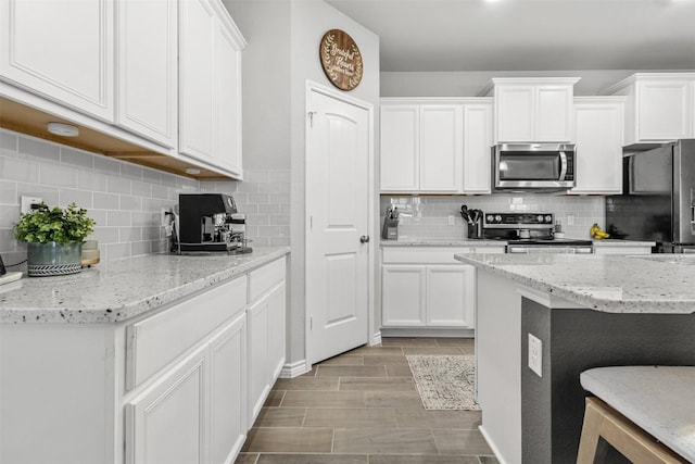 5867 Copano Loop, Belton, TX 76513 - kitchen with appliances with stainless steel finishes, tasteful backsplash, white cabinetry, light stone counters, and a breakfast bar