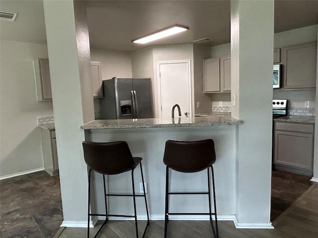 2101 Whistling Way, Taylor, TX 76574 - kitchen with stainless steel appliances, a breakfast bar area, light stone counters, and a peninsula