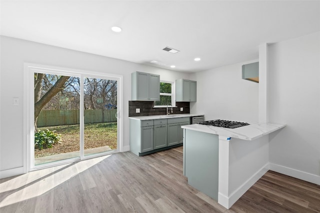 9417 N Creek Dr, Austin, TX 78753 - kitchen with gray cabinetry, light wood-style flooring, decorative backsplash, black gas cooktop, and a peninsula
