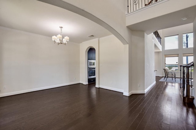 2521 Blended Tree Ranch Dr, Leander, TX 78641 - spare room featuring a chandelier, arched walkways, dark wood-type flooring, ornamental molding, and a towering ceiling