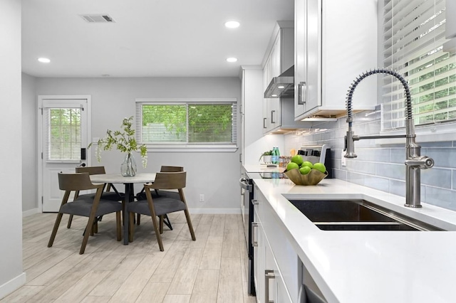11508 Bell Ave, Austin, TX 78759 - kitchen with stainless steel range with electric cooktop, backsplash, wall chimney exhaust hood, light countertops, and light wood-style flooring