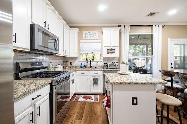 14908 Chamomile Cv, Pflugerville, TX 78660 - kitchen with stainless steel appliances, ornamental molding, a center island, a kitchen breakfast bar, and wood finished floors