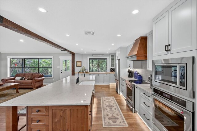 23644 Nameless Rd, Leander, TX 78641 - kitchen with appliances with stainless steel finishes, premium range hood, a spacious island, light stone countertops, and recessed lighting