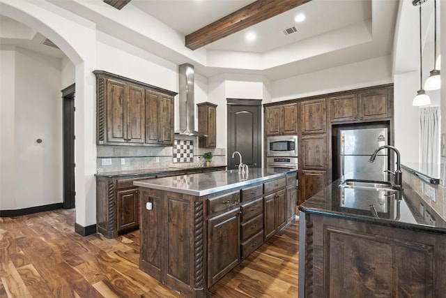 1310 Minnie Dr, Austin, TX 78732 - kitchen featuring wall chimney exhaust hood, a kitchen island with sink, appliances with stainless steel finishes, tasteful backsplash, and dark brown cabinets
