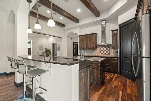 1310 Minnie Dr, Austin, TX 78732 - kitchen featuring freestanding refrigerator, wall chimney exhaust hood, arched walkways, dark wood-type flooring, and a kitchen island with sink