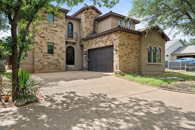 1310 Minnie Dr, Austin, TX 78732 - mediterranean / spanish house featuring stone siding, stucco siding, a balcony, concrete driveway, and a garage