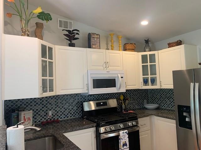 6004 Blythewood Dr, Austin, TX 78745 - kitchen with stainless steel appliances, decorative backsplash, white cabinetry, glass insert cabinets, and vaulted ceiling