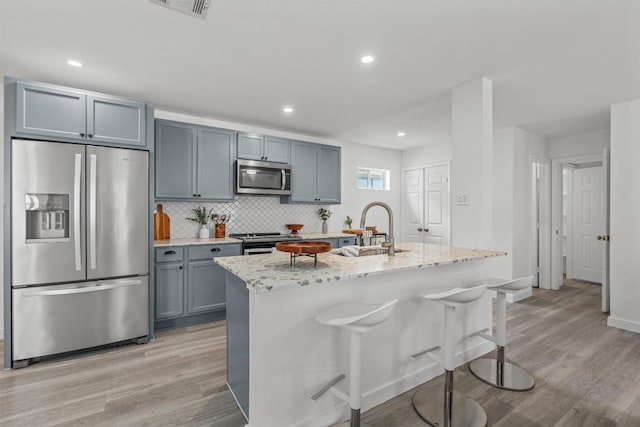837 Mica Ln, Leander, TX 78641 - kitchen with stainless steel appliances, light wood-style floors, light stone counters, backsplash, and a center island with sink