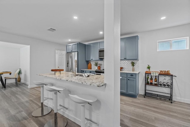 837 Mica Ln, Leander, TX 78641 - kitchen with appliances with stainless steel finishes, a kitchen breakfast bar, light wood-style floors, recessed lighting, and tasteful backsplash