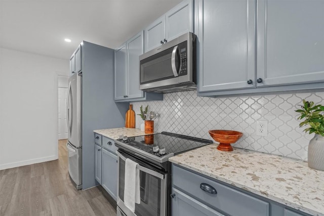837 Mica Ln, Leander, TX 78641 - kitchen featuring appliances with stainless steel finishes, wood finished floors, decorative backsplash, gray cabinetry, and light stone counters