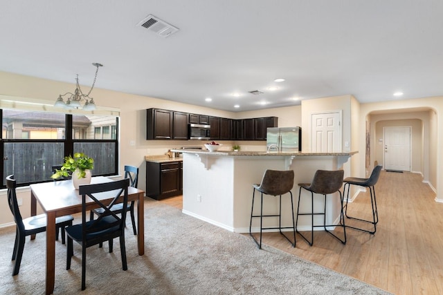 913 Mahomet Dr, Pflugerville, TX 78660 - kitchen featuring appliances with stainless steel finishes, a kitchen bar, arched walkways, dark brown cabinetry, and an island with sink