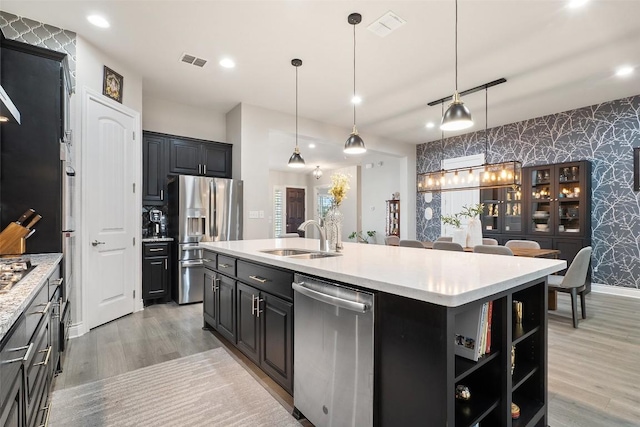 225 Escarpment Way, Cedar Park, TX 78613 - kitchen featuring stainless steel appliances, wallpapered walls, light wood-type flooring, a kitchen island with sink, and open shelves