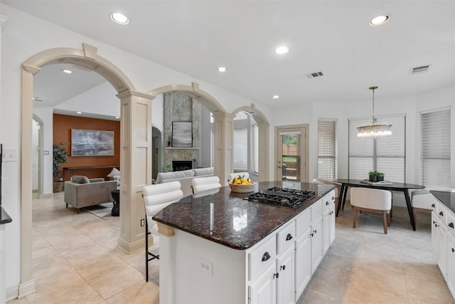 7608 Journeyville Dr, Austin, TX 78735 - kitchen with black gas cooktop, a tile fireplace, hanging light fixtures, arched walkways, and white cabinets