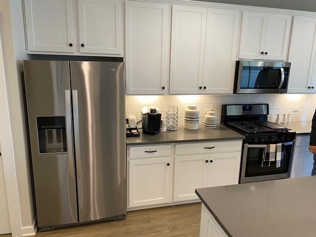 303 Watercourse Way, Bastrop, TX 78602 - kitchen featuring appliances with stainless steel finishes, backsplash, white cabinetry, dark countertops, and light wood-type flooring