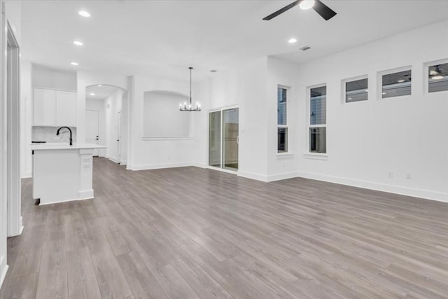 8609 San Giano Cv, Round Rock, TX 78665 - unfurnished living room with a ceiling fan, a chandelier, recessed lighting, wood finished floors, and arched walkways
