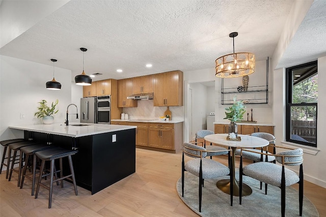 506 Explorer, Lakeway, TX 78734 - kitchen featuring a textured ceiling, under cabinet range hood, stainless steel appliances, light wood-style flooring, and a peninsula