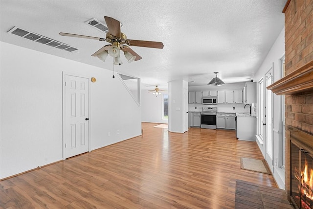 506 Turtle Back Cv, Killeen, TX 76542 - unfurnished living room with a fireplace, a ceiling fan, light wood-type flooring, and a textured ceiling