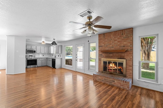 506 Turtle Back Cv, Killeen, TX 76542 - unfurnished living room featuring a textured ceiling, wood finished floors, a ceiling fan, and a brick fireplace