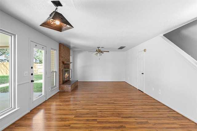 506 Turtle Back Cv, Killeen, TX 76542 - unfurnished living room featuring wood finished floors, a ceiling fan, a brick fireplace, and a textured ceiling