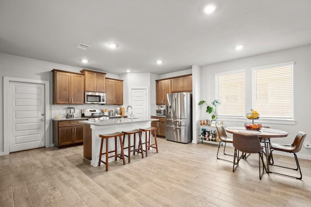 2705 Grizzly Way, Leander, TX 78641 - kitchen with appliances with stainless steel finishes, a kitchen bar, light wood-style flooring, an island with sink, and brown cabinetry