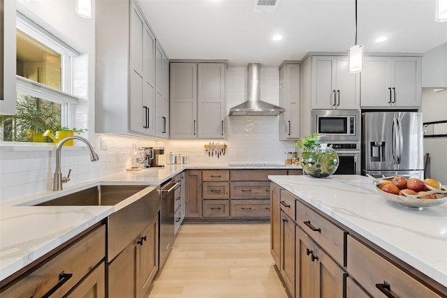106 Samantha Ln, Kingsland, TX 78639 - kitchen with appliances with stainless steel finishes, wall chimney exhaust hood, gray cabinetry, light wood-style floors, and backsplash