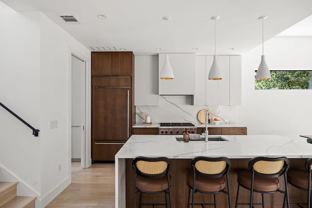1911 Piedmont Ave, Austin, TX 78757 - kitchen featuring modern cabinets, a breakfast bar, backsplash, decorative light fixtures, and light wood finished floors