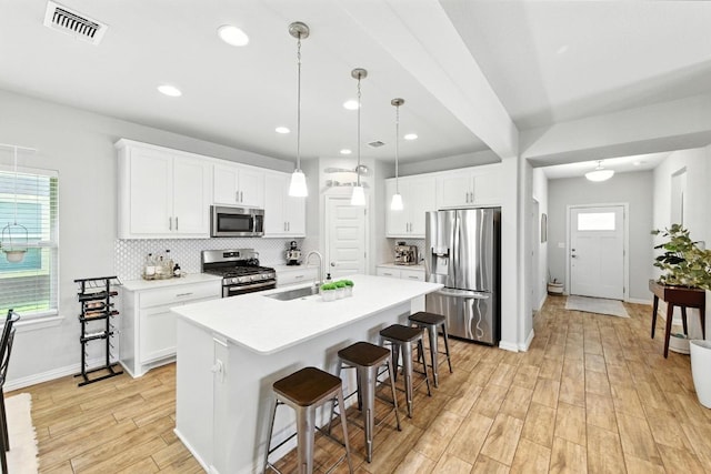 5512 Baythorne Dr, Austin, TX 78747 - kitchen with appliances with stainless steel finishes, a center island with sink, light wood-style flooring, tasteful backsplash, and a kitchen breakfast bar