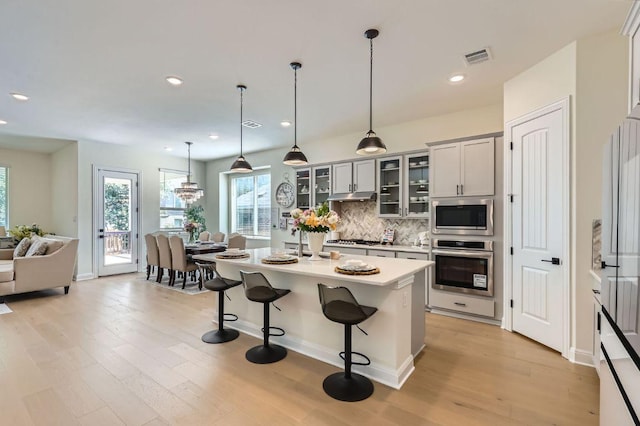 1505 Sibley Way, Leander, TX 78641 - kitchen featuring stainless steel appliances, light wood finished floors, backsplash, a breakfast bar area, and glass insert cabinets