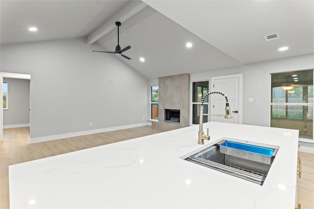 3907 Carmel Dr, Austin, TX 78721 - kitchen featuring light wood-type flooring, beam ceiling, a ceiling fan, a large fireplace, and open floor plan