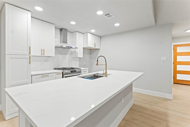 3907 Carmel Dr, Austin, TX 78721 - kitchen with wall chimney exhaust hood, stainless steel gas range oven, white cabinets, light wood finished floors, and recessed lighting