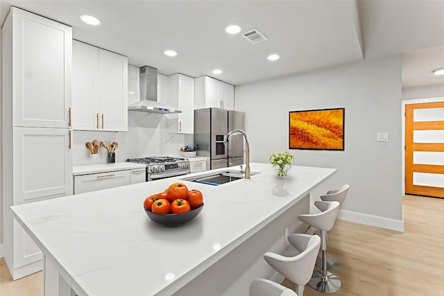 3907 Carmel Dr, Austin, TX 78721 - kitchen with wall chimney exhaust hood, stainless steel appliances, light wood finished floors, white cabinets, and recessed lighting