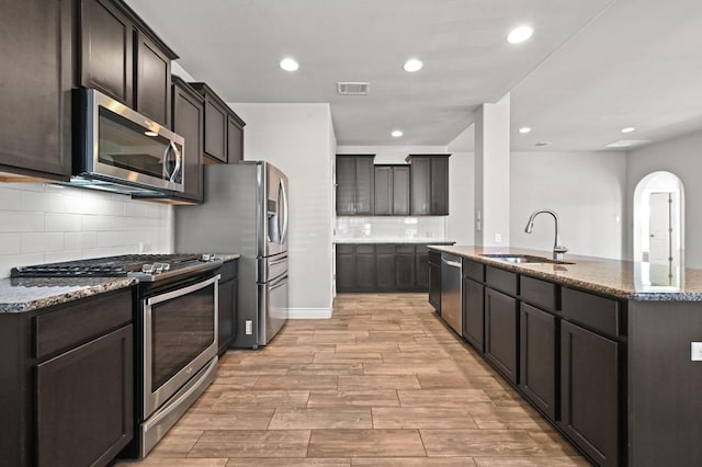 19113 Melwas Way, Pflugerville, TX 78660 - kitchen with appliances with stainless steel finishes, dark stone counters, arched walkways, light wood-style floors, and backsplash