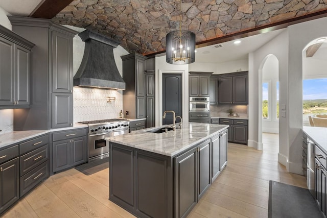 1216 Travis Bluff Way, Spicewood, TX 78669 - kitchen featuring stainless steel appliances, custom exhaust hood, light wood finished floors, and arched walkways