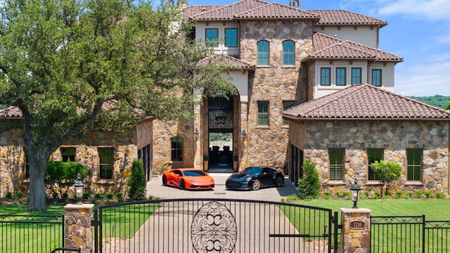 1216 Travis Bluff Way, Spicewood, TX 78669 - mediterranean / spanish-style house with a gate, stone siding, stucco siding, a tile roof, and driveway