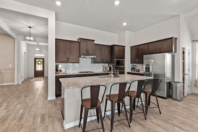 232 Silver Pass, Kyle, TX 78640 - kitchen featuring stainless steel appliances, dark brown cabinetry, light wood finished floors, a breakfast bar, and backsplash