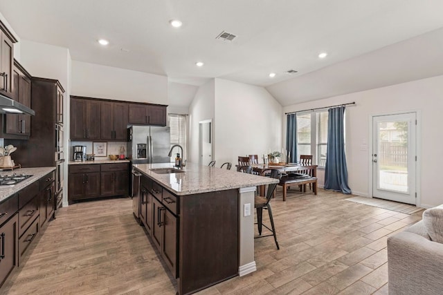 232 Silver Pass, Kyle, TX 78640 - kitchen featuring a kitchen bar, lofted ceiling, dark brown cabinetry, a kitchen island with sink, and light stone countertops