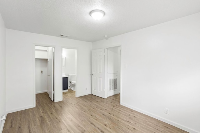 3050 Beacon Fld, San Antonio, TX 78245 - unfurnished bedroom with light wood finished floors, a spacious closet, a textured ceiling, a closet, and connected bathroom