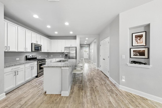 9108 Alex Ln, Austin, TX 78748 - kitchen with stainless steel appliances, white cabinets, light wood-style floors, recessed lighting, and a center island with sink
