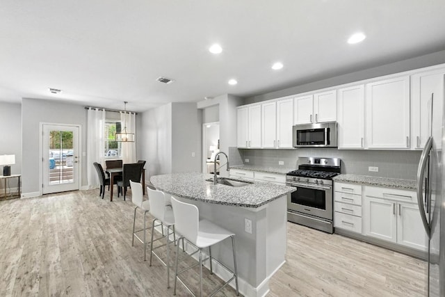 9108 Alex Ln, Austin, TX 78748 - kitchen featuring stainless steel appliances, tasteful backsplash, light wood-type flooring, white cabinetry, and light stone counters
