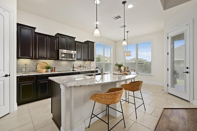 1113 Hartman Dr, Leander, TX 78641 - kitchen featuring stainless steel microwave, a breakfast bar area, light stone countertops, backsplash, and light tile patterned floors