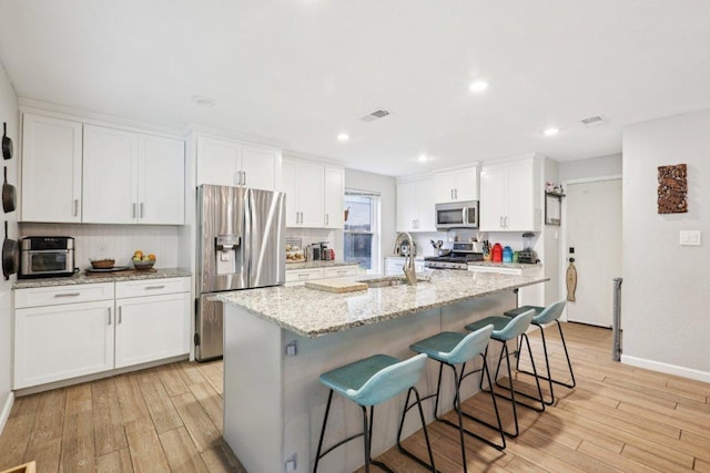 6803 Moonmont Dr, Austin, TX 78745 - kitchen featuring appliances with stainless steel finishes, light wood finished floors, white cabinets, a kitchen breakfast bar, and a center island with sink