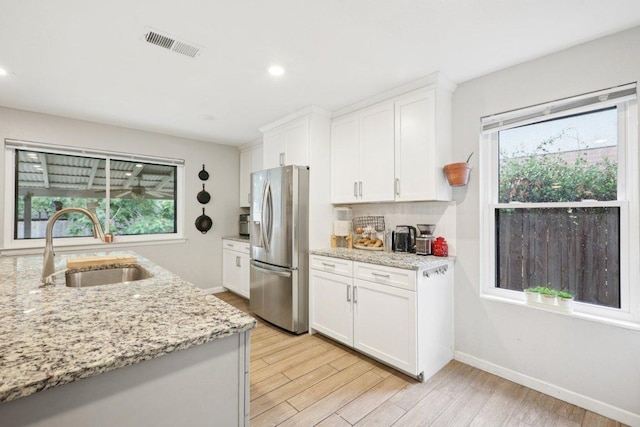 6803 Moonmont Dr, Austin, TX 78745 - kitchen featuring stainless steel refrigerator with ice dispenser, healthy amount of natural light, white cabinets, light wood finished floors, and recessed lighting