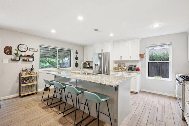 6803 Moonmont Dr, Austin, TX 78745 - kitchen with stainless steel appliances, light wood-style flooring, a breakfast bar, a center island with sink, and white cabinets